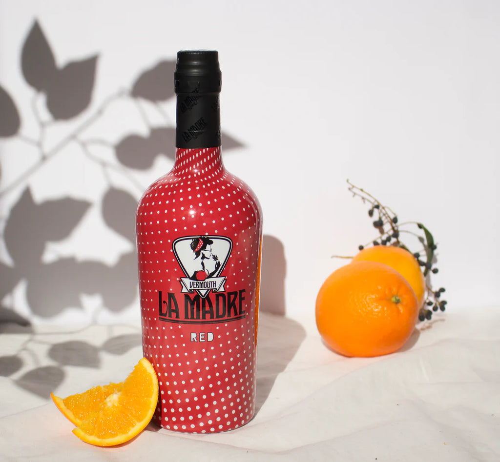 VERMUT ROJO LA MADRE 75 cl bottle in red with white dots, next to fresh orange and orange slice on white surface.